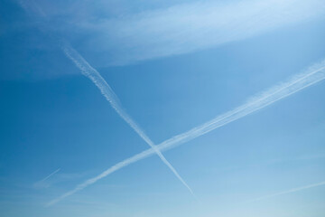 Clear blue sky with intersecting airplane contrails forming an X shape.