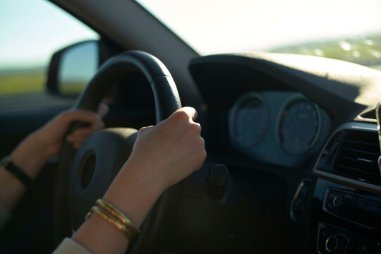 Hands firmly grip the steering wheel inside a sunlit car on an open road.