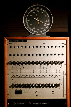 Retro control panel with switches and dials under an analog clock in dim lighting.