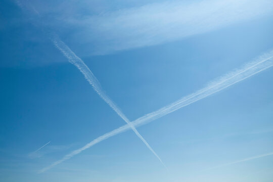 Clear blue sky with intersecting airplane contrails forming an X shape.