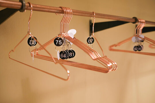 Copper hangers on a rod with numbered keychains attached in a well-lit room.