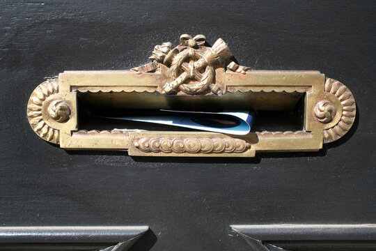 A letter partially sticking out of an ornate, gold-colored door mail slot.