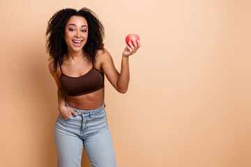Happy woman in casual wear holding a red apple against beige background