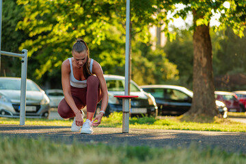 Young sportswoman tying her shoelaces on sneakers, preparing for a workout session at an outdoor...