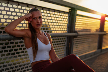 Athletic woman resting against a metal fence during sunset, showcasing strength and determination....