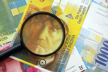 Swiss franc banknotes and magnifying glass. The current francs money bills with loupe lies on table