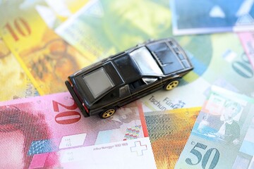 Swiss franc banknotes and toy car. The current francs money bills and black car lies on table