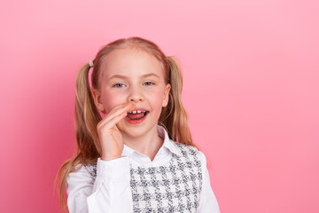 Charming schoolgirl with ponytails making a cheerful expression against a bright pink background in formal school uniform