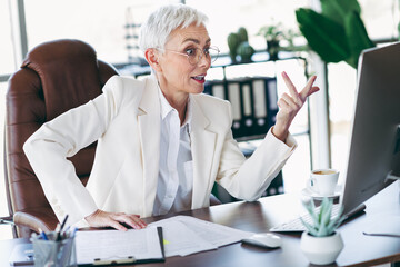 Fototapeta premium Mature businesswoman working in an office environment, engaging in an online meeting, situated in an elegant workplace