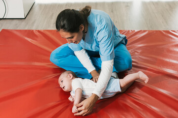 Physiotherapist assisting baby with rolling exercises on red mat