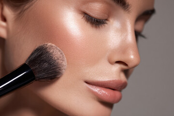 Close up shot of woman face showcasing flawless complexion, highlighting application of makeup with soft brush. image captures elegance and precision of beauty routines, evoking sense of luxury