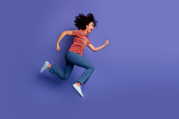 Happy young woman jumping joyfully in casual fashion against a purple background, expressing...