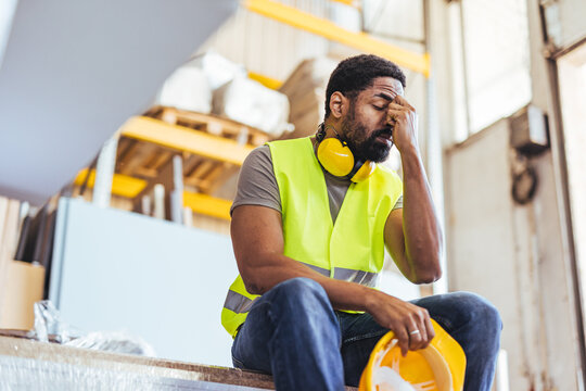 Tired Industrial Worker Sitting in Warehouse Wearing Safety Gear