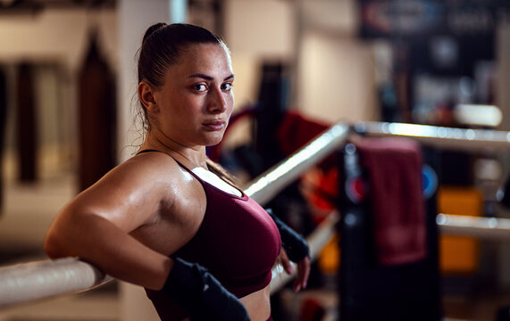 Female boxer leaning against the ropes of a boxing ring resting after training looking at camera. - Powered by Adobe