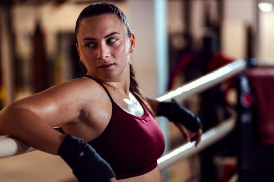 Female boxer leaning against the ropes of a boxing ring resting after training. - Powered by Adobe
