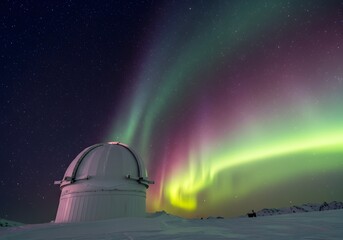 Majestic aurora borealis display over a snow-covered observatory dome.