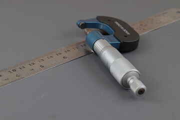 A blue screw micrometer and iron ruler isolated on grey background, A micrometer is a tool to...