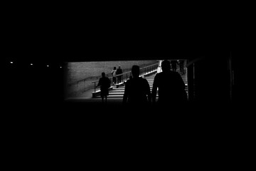 Silhouetted commuters leave a dark pedestrian underpass in Rome, Italy, climbing sunlit steps...