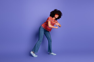 Cheerful young woman wearing trendy attire posing against a vibrant purple background, showing lively and happy gestures