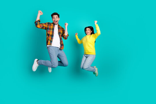 Young joyful couple jumping together against teal background expressing enthusiasm and happiness, celebrating positive moments
