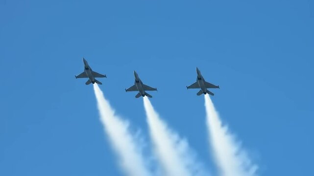 Three fighter jets performing a synchronized aerial display against a clear blue sky, showcasing precision