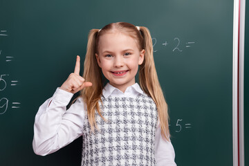 Smiling schoolgirl with blonde ponytails raises hand in classroom showcasing knowledge during a lesson