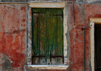 Rustic green shutter on weathered red wall with rustic textures