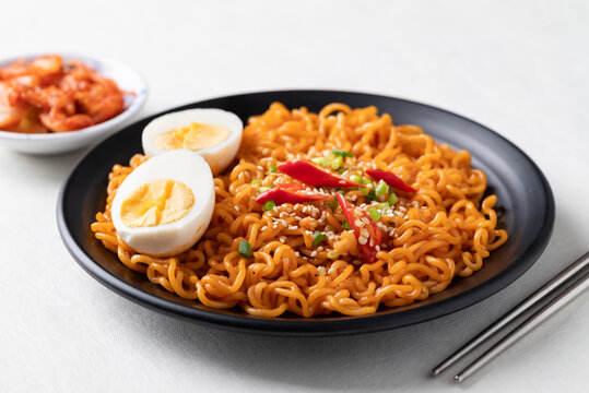 Spicy Korean dried instant noodles with boiled egg, sliced scallions, sesame seed, fresh chili and kimchi on white background, Korean ramyeon