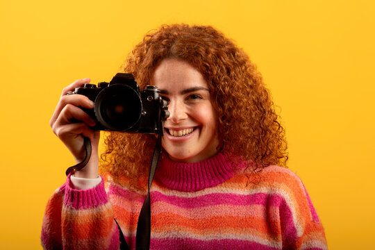 Redhead photographer taking pictures with vintage camera smiling on yellow background - Powered by Adobe