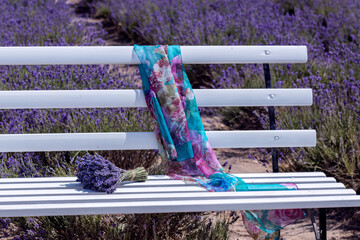 Lavender bouquet and colorful scarf on white bench in a field. Countryside travel and relaxation concept. Summer nature scene.
