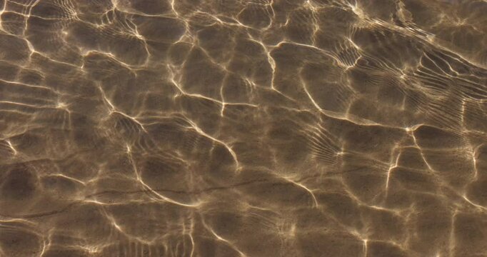Mesmerising natural patterns of crystal clear ocean water glistening in the shallows of an idyllic clean shoreline. Captured from above in slow motion.