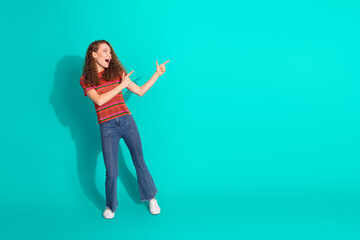 Fashionable young woman in casual attire posing with expressive hand gesture against a vibrant teal background