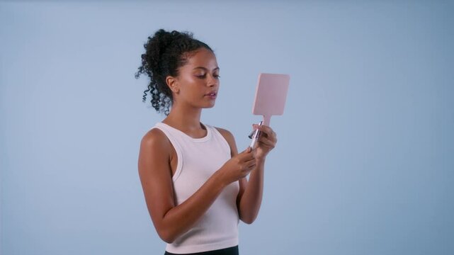 Model carefully applies lipstick while looking in a mirror, then smiles warmly at the camera.