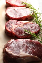 Pieces of raw beef meat and rosemary on parchment paper, closeup