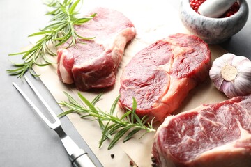 Pieces of raw beef meat, spices and carving fork on grey table, closeup