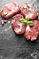 Pieces of raw beef meat and basil on dark table, flat lay. Space for text