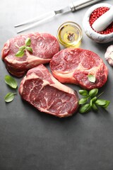 Pieces of raw beef meat, spices and carving fork on grey table, flat lay. Space for text