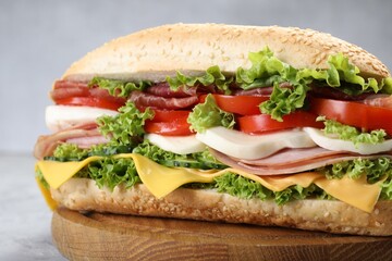 Tasty baguette sandwich with ham, cheese and vegetables on grey table, closeup