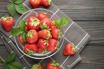 Fresh ripe strawberries and leaves in container on black wooden table, flat lay. Space for text