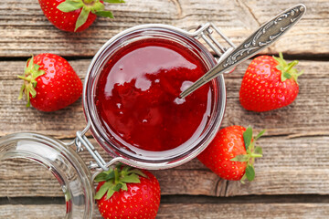 Tasty strawberry jam in glass jar and fresh berries on wooden table, flat lay