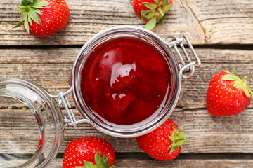 Tasty strawberry jam in glass jar and fresh berries on wooden table, flat lay