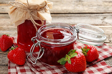 Tasty strawberry jam in glass jars and fresh berries on wooden table, closeup