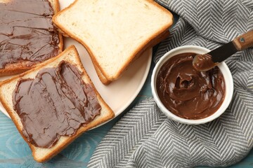 Tasty chocolate butter in bowl, slices of bread and knife on light blue wooden table, flat lay