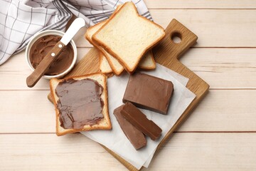 Tasty chocolate butter, slices of bread and knife on light wooden table, flat lay