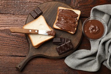Tasty chocolate butter, pieces, knife and slices of bread on wooden table, flat lay