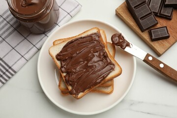 Slices of bread with tasty chocolate butter and knife on white marble table, flat lay