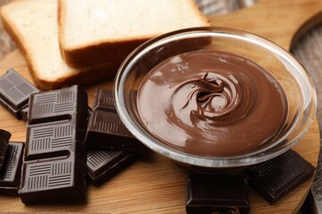Tasty chocolate butter in glass bowl, pieces and bread on table, closeup