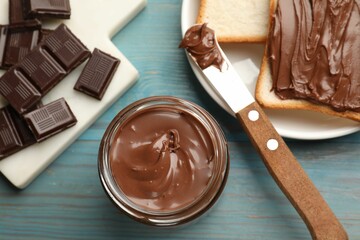 Tasty chocolate butter, pieces, knife and slices of bread on light blue wooden table, flat lay