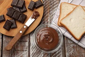Tasty chocolate butter, pieces, knife and slices of bread on color wooden table, flat lay