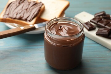 Tasty chocolate butter in glass jar on light blue wooden table, closeup